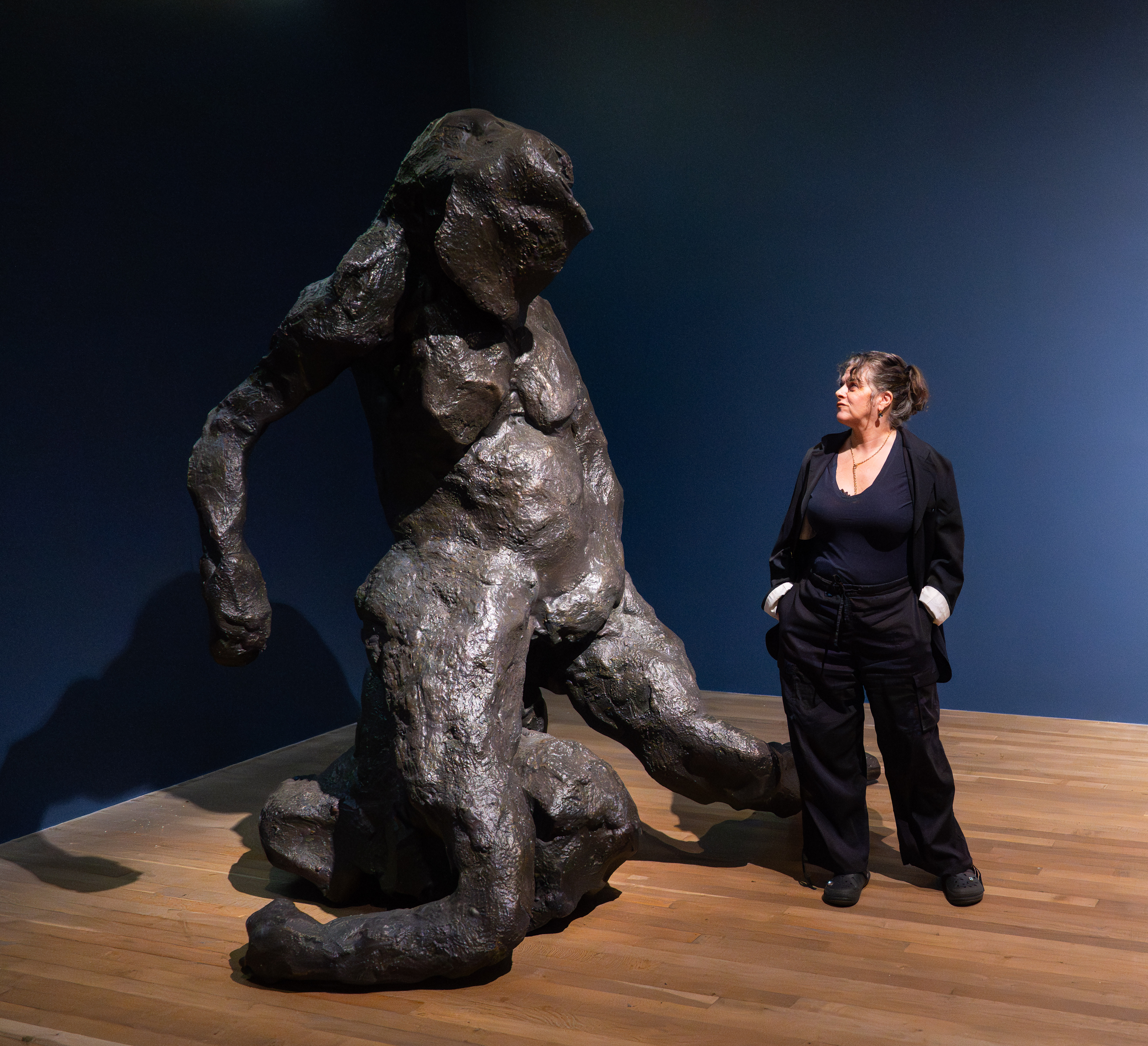 Tracey Emin stands next to her large, dark bronze sculpture of a crouching figure.