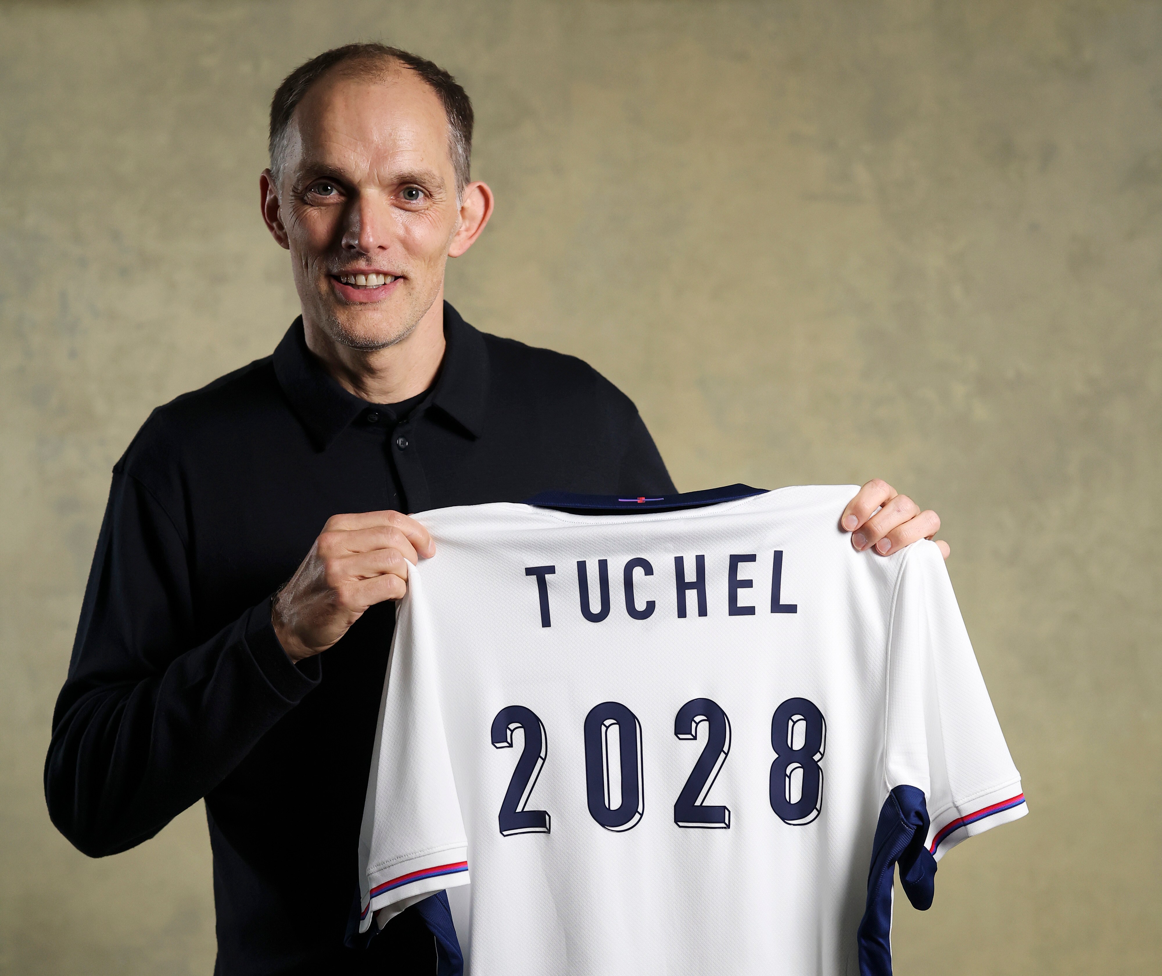 England manager Thomas Tuchel holding a jersey with "TUCHEL 2028" on the back, indicating his contract extension.