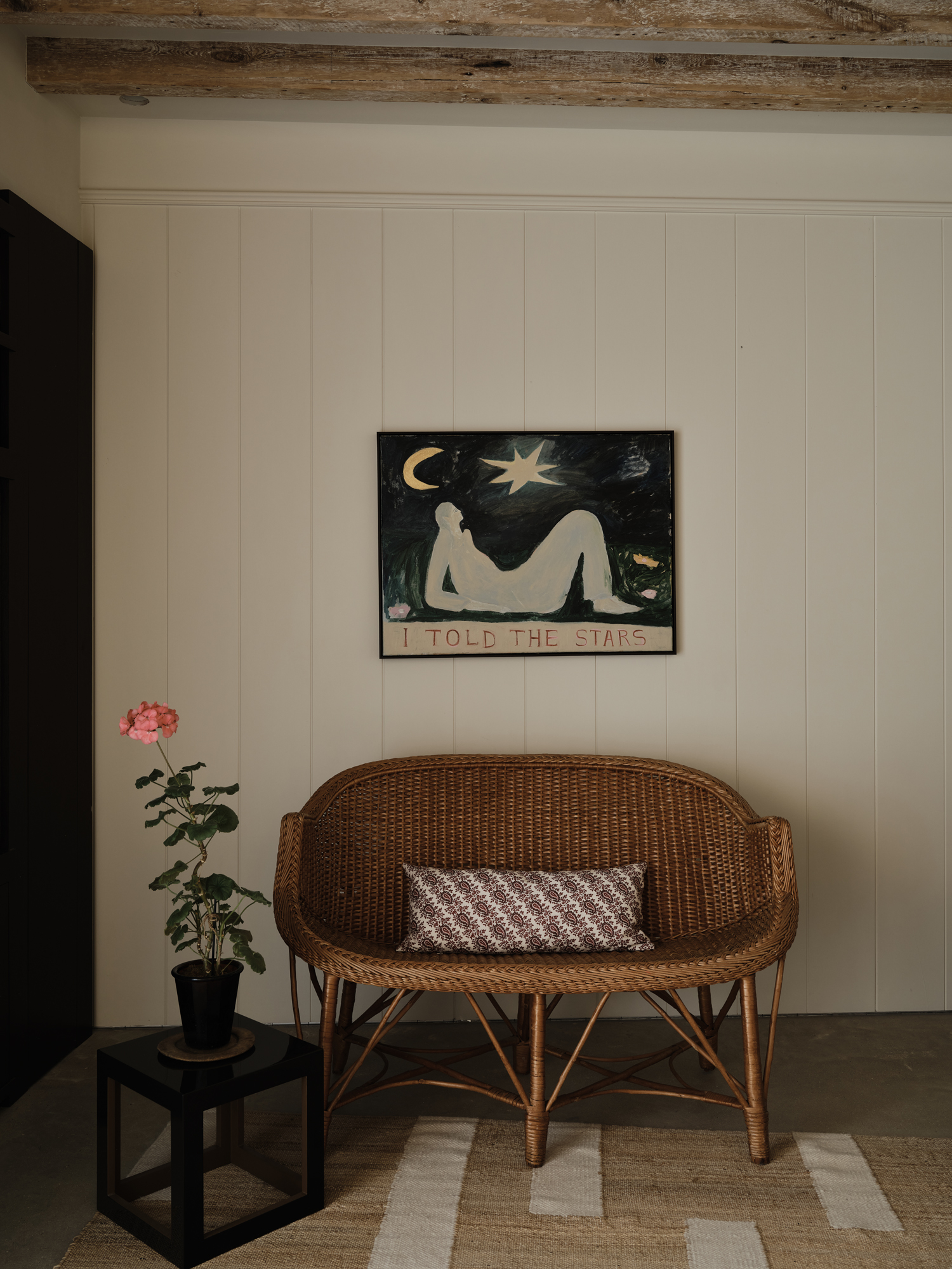 A painting depicting a figure looking up at the moon and stars, above a wicker loveseat.