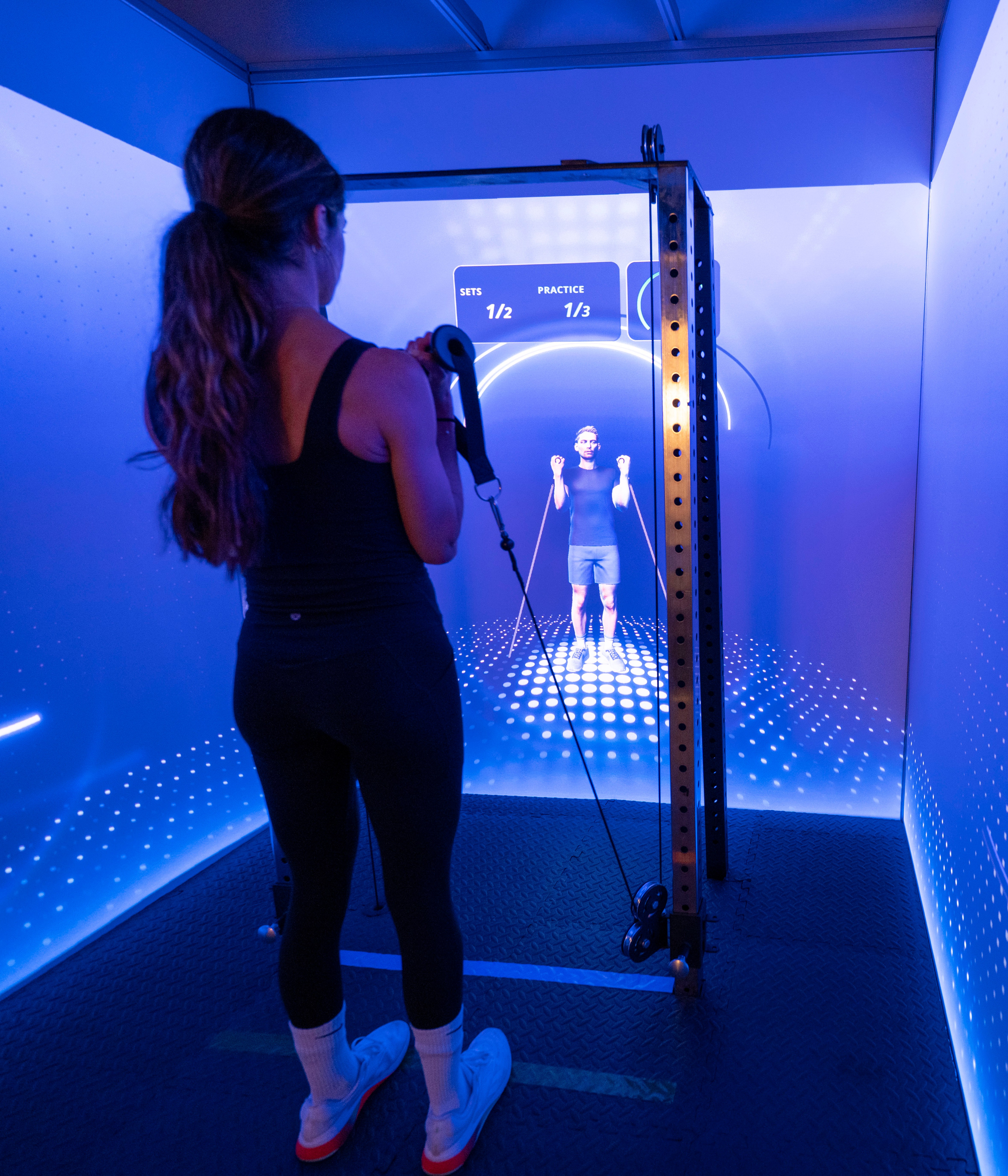 A woman training in a smart gym cube with interactive projection screens and digital weights.