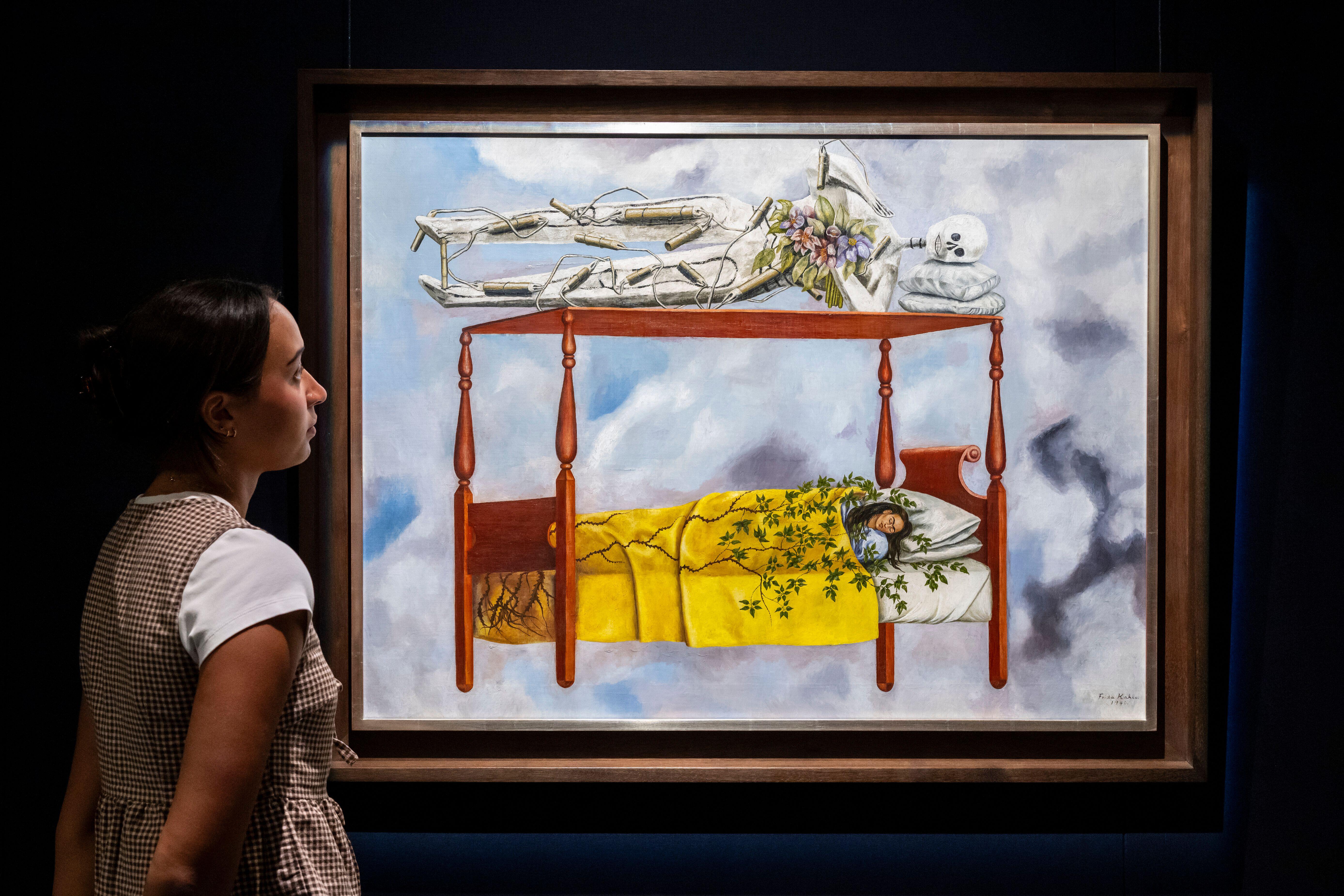 "El sueño (La cama)" by Frida Kahlo, a painting depicting a sleeping figure on a bed and a skeletal figure on a structure above it, on display.