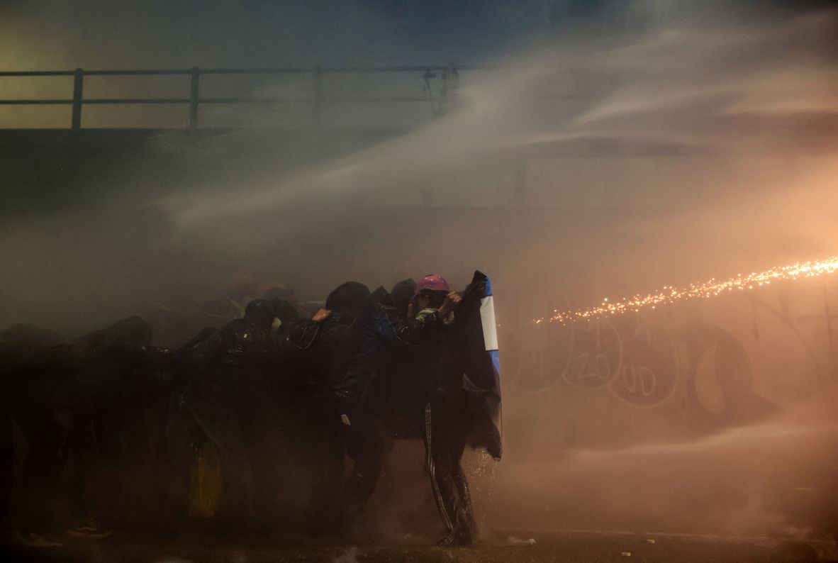 Anti-Olympic protesters take cover as police use a water cannon against them in Milan on February 7. Protesters marched peacefully through the city during the afternoon. But when night fell, <a href=