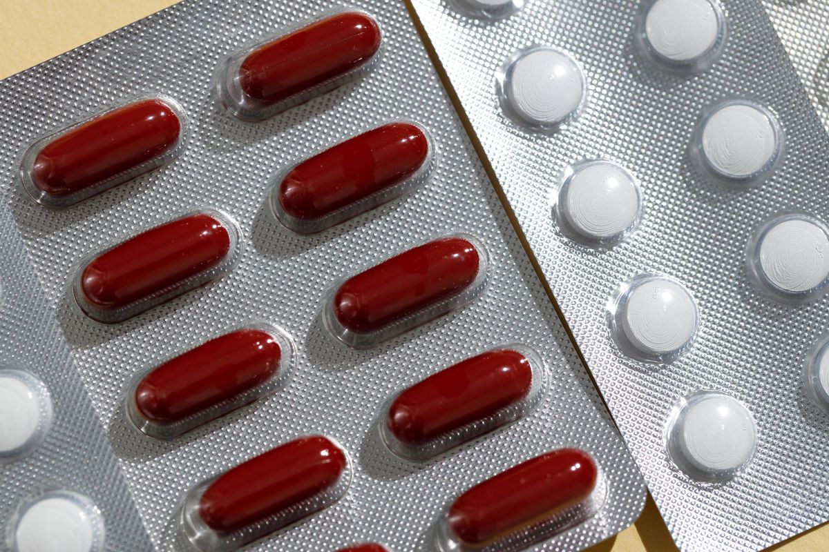Close-up of blisters with red and white pills and capsules on beige background.