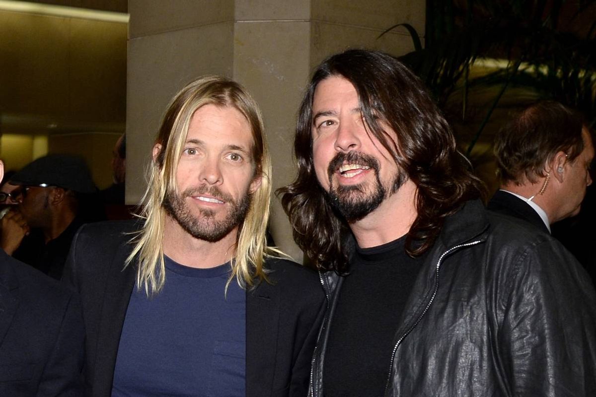 Two individuals with long hair and beards standing close to each other, smiling and posing for a photograph.