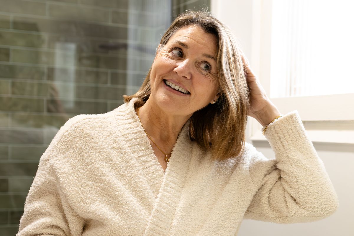 Smiling senior woman wearing bathrobe, looking at herself in the mirror and fixing her hair in the bathroom