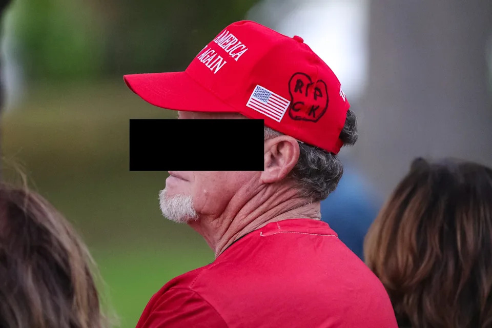 Man wearing a baseball cap and T-shirt with American flag attending a sports event outdoors