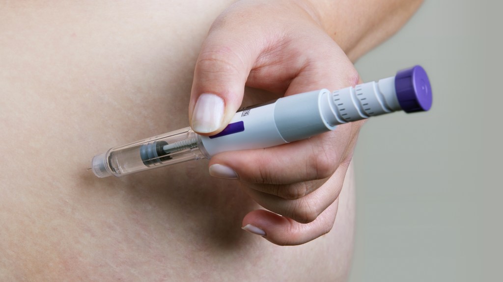 A person injecting their abdomen with a Mounjaro or GLP-1 injector pen.