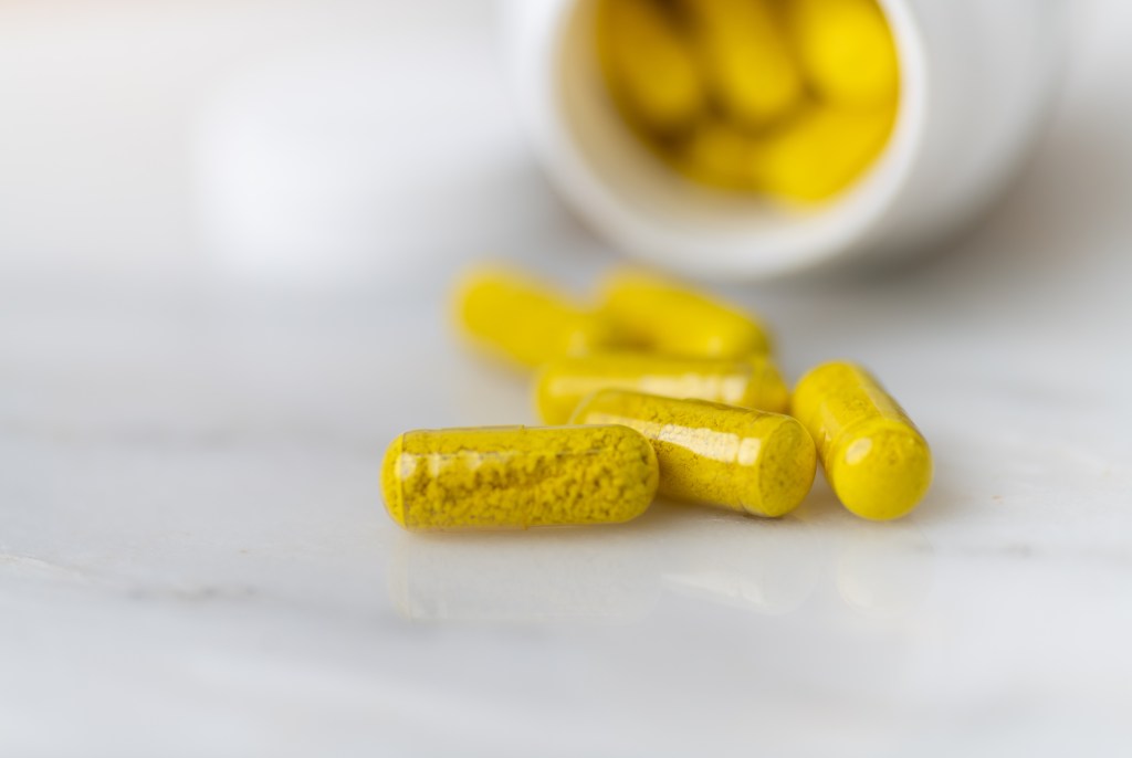 Yellow berberine capsules spilled from a white bottle.