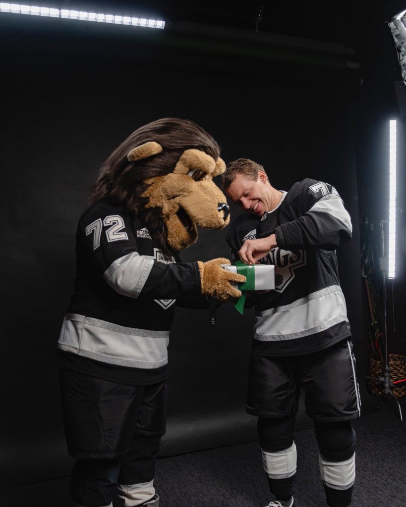 Artemi Panarin, in a black and white jersey, opens a gift box held by the Kings mascot, who is also wearing a black and white jersey with "72" on it.