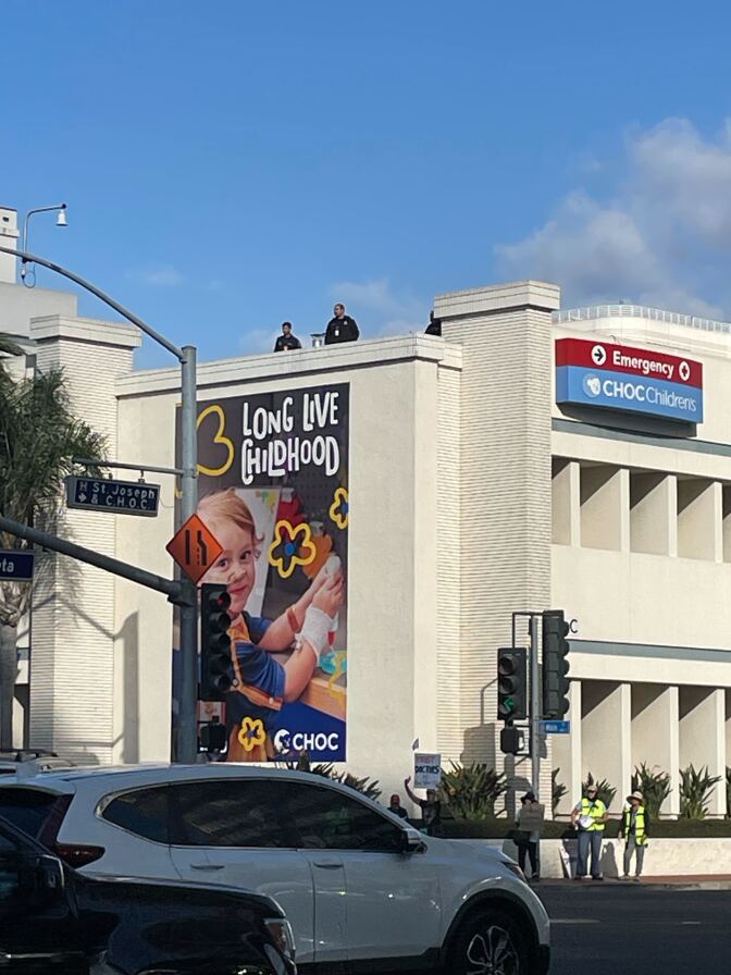 Two security guards standing on the roof of a building. You can see a sign that says "CHOC Children's" and a large mural that says "Long live childhood."
