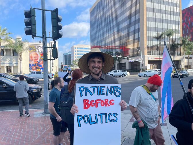 A man poses at a rally with a sign that says "patients before politics."