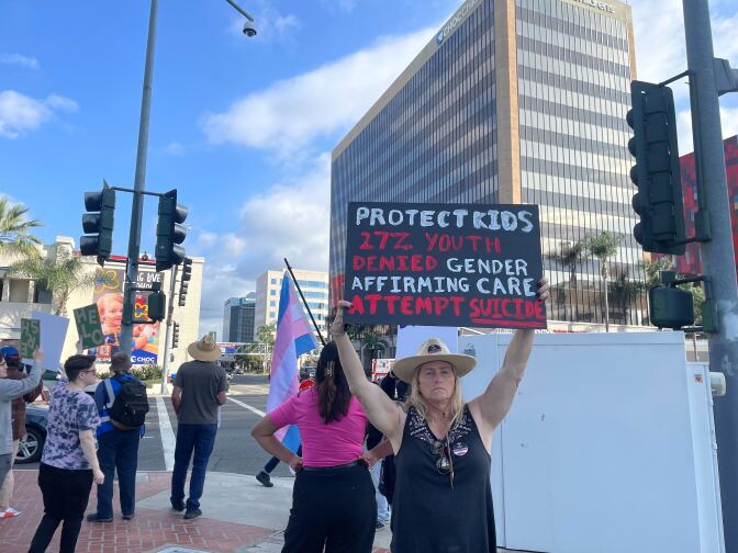 A woman holds up a sign that says "Protect kids, 27% youth denied gender affirming care attempt suicide."