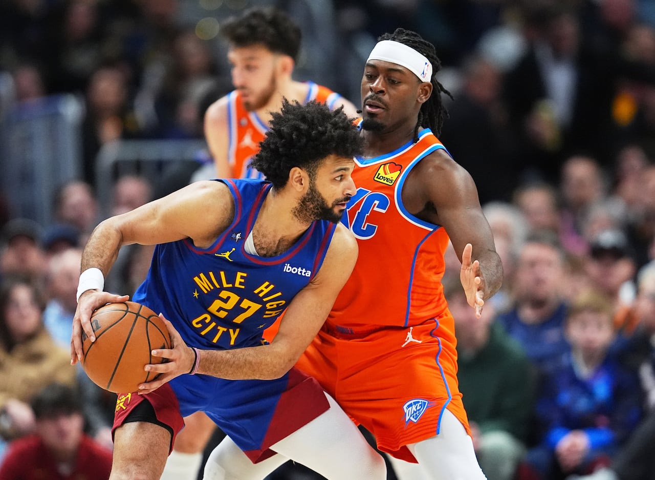 Three basketball players, two in focus and one in a blue jersey that says "mile high city" has the ball looking to pass, in an NBA game
