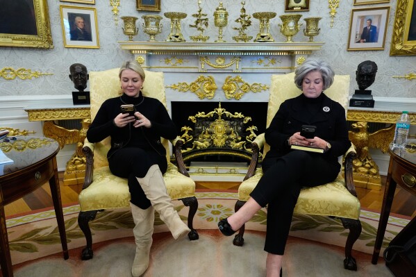 Press secretary Karoline Leavitt and chief of staff Susie Wiles check their phones as President Donald Trump speaks in the Oval Office of the White House in Washington, Feb. 2, 2026. (AP Photo/Alex Brandon, File)