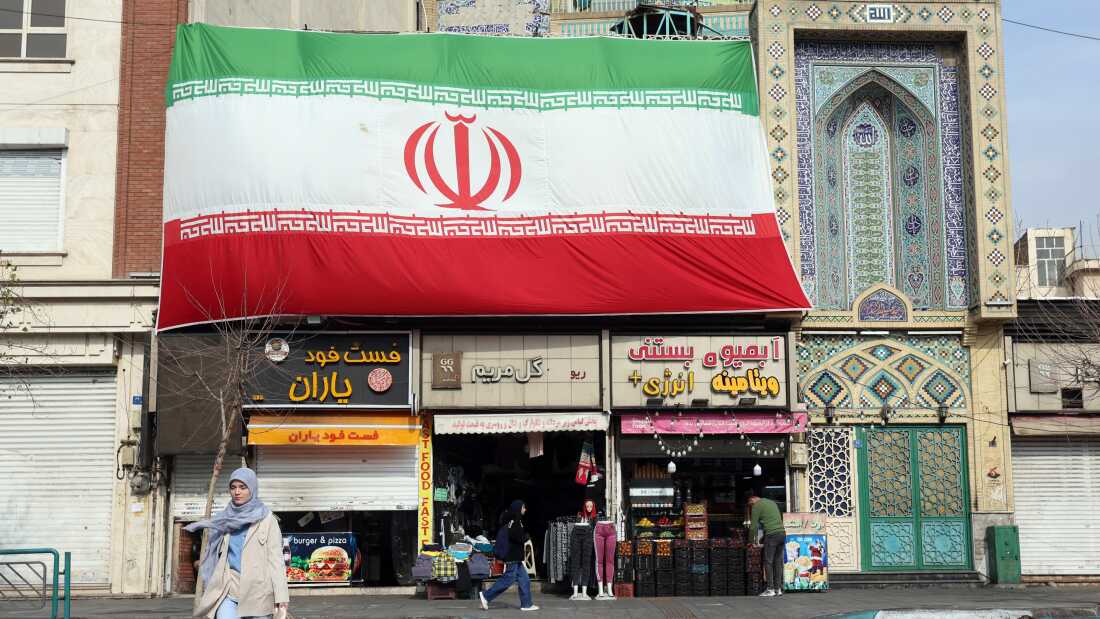 An Iranian woman walks past a huge national flag hanging above shops, in Tehran on Febr. 6.