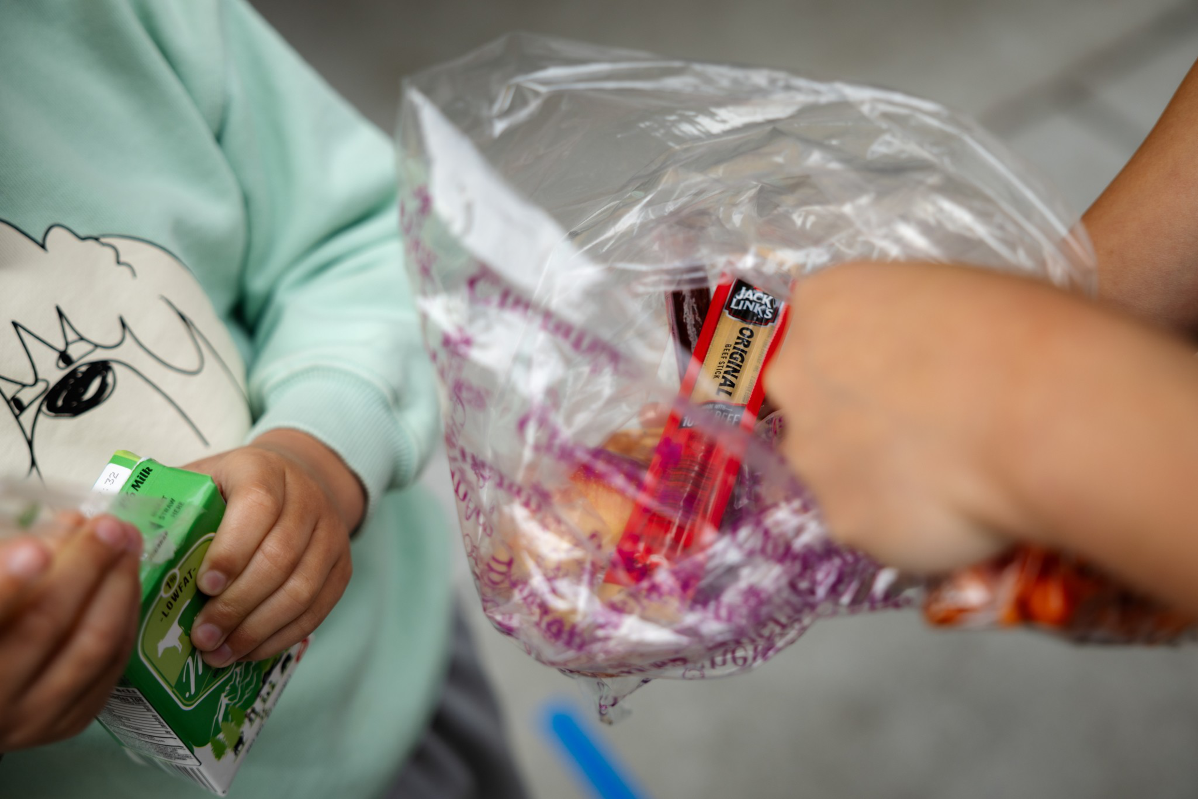 Two people are holding a juice box and a clear plastic bag containing snack items, including a Jack Link’s Original beef jerky stick.
