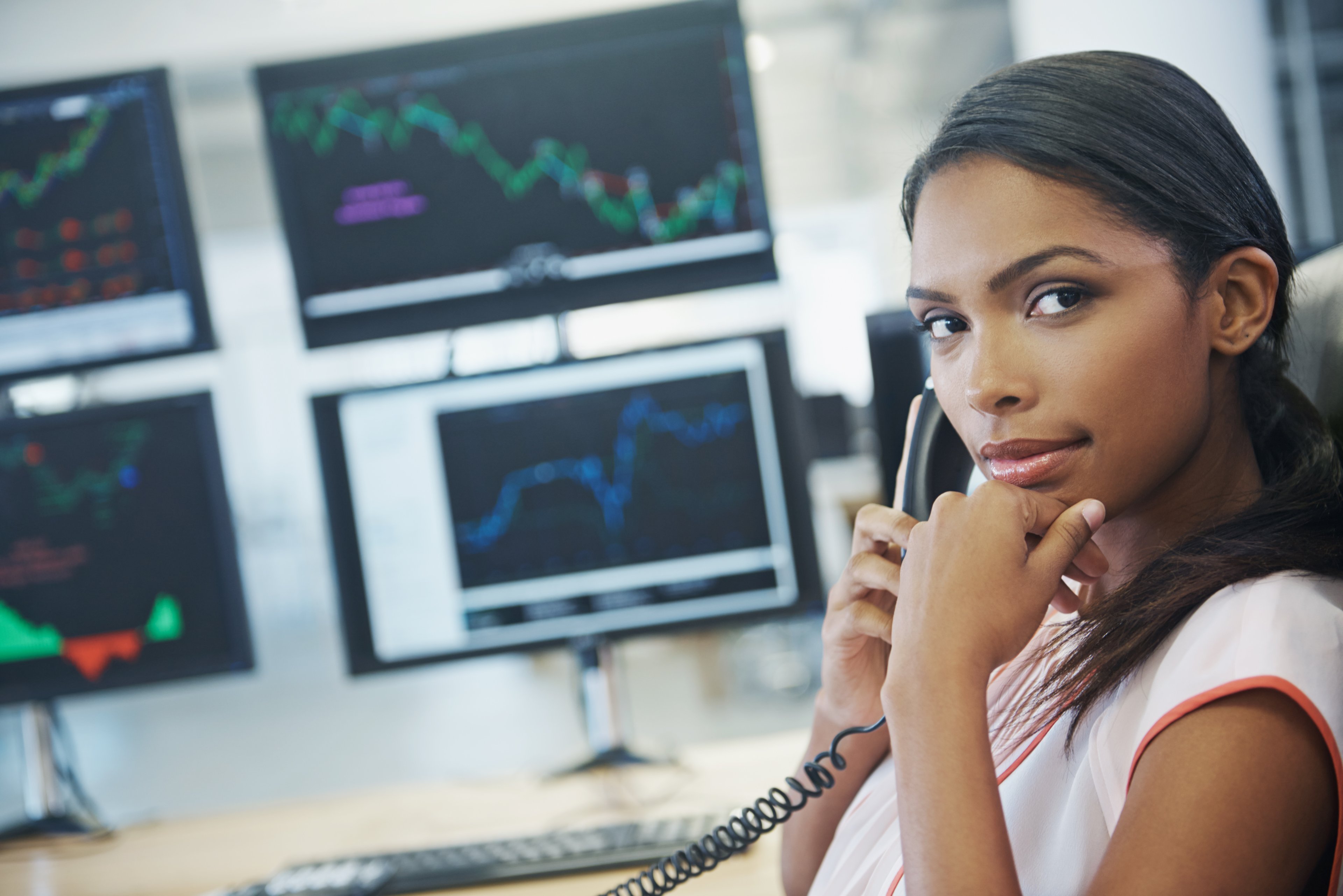 A trader on the phone with computer screen filled with stock data behind them. 