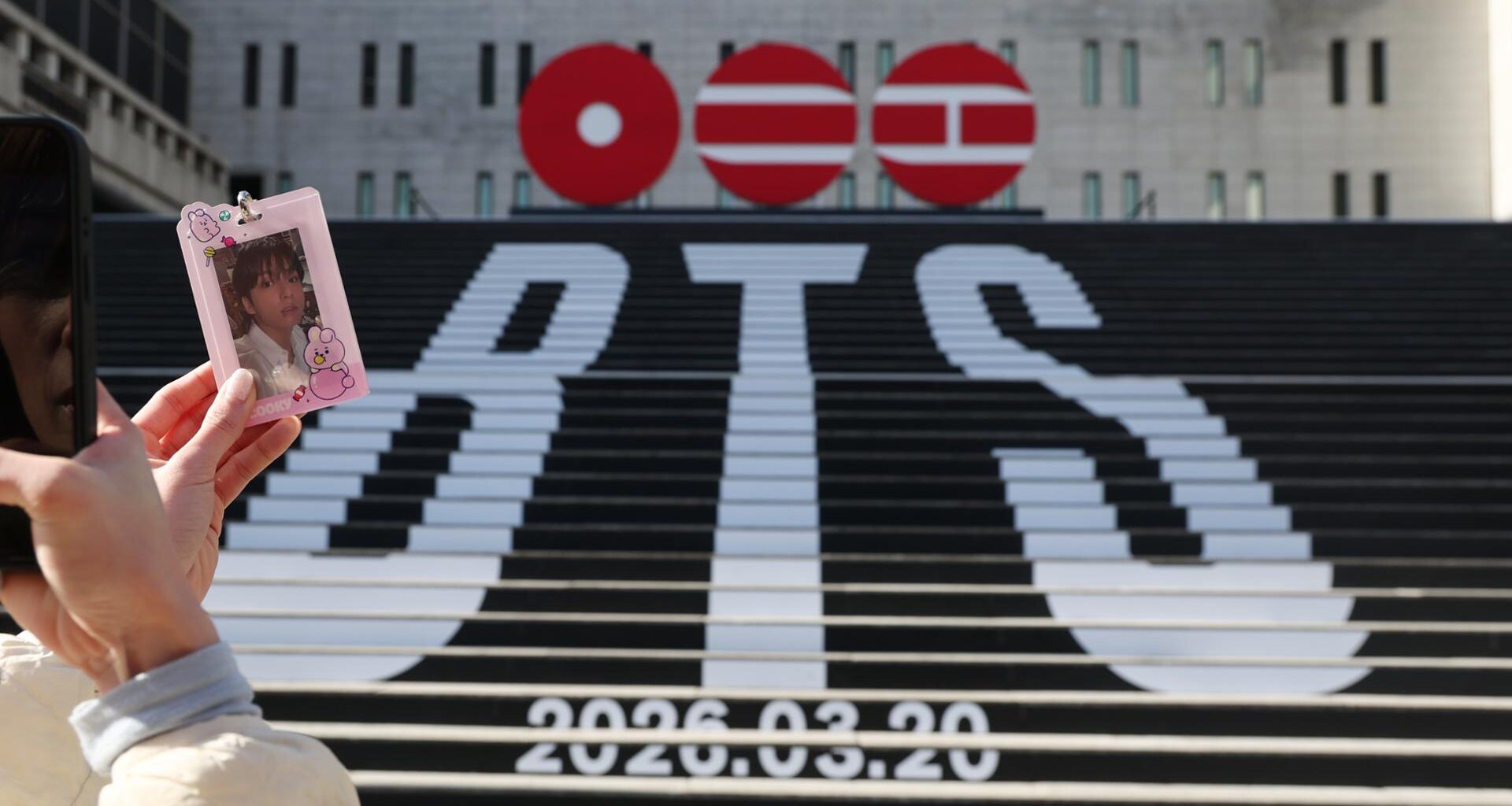 A visitor takes a picture of a photocard in front of a street installation promoting K-pop boy band BTS