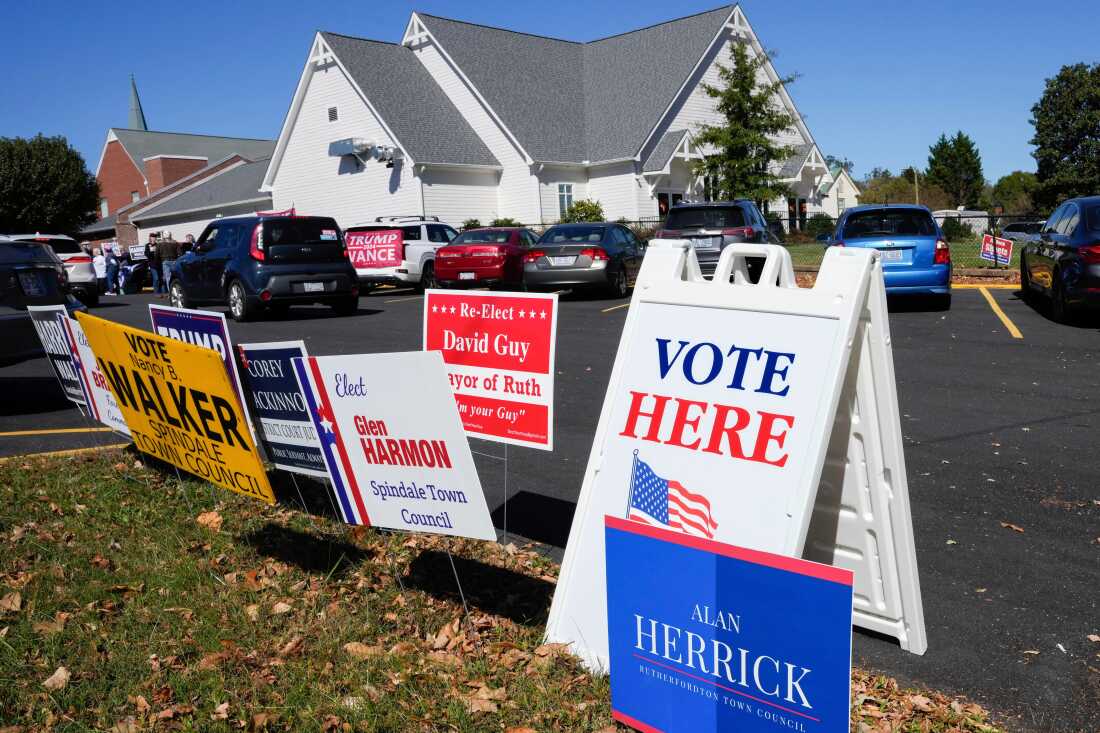 A Vote Here sign is posted amongst political signs as people arrive to vote at the Rutherford County Annex Building, an early voting site, Oct. 17, 2024, in Rutherfordton, N.C.