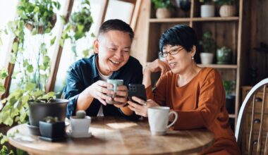 A happy retired couple smiles and drinks coffee while sitting at their kitchen table with plants next to them