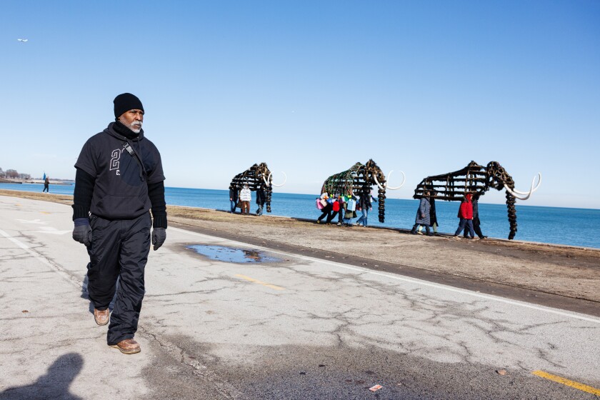 Nick Cave (left) walks alongside dancers donning the mammoth costume as they walk to a location for the video portion of “Nick Cave: Mammoth” a series by artist Nick Cave during a video shoot near the Theater by the Lake at North DuSable Lakeshore Drive and West Fullerton Parkway on the lakefront, Tuesday, Jan. 13, 2026.