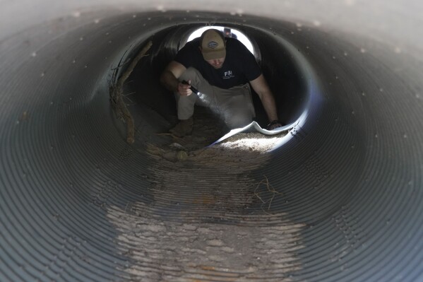 An investigator searches inside a culvert in the neighborhood where Annie Guthrie, whose mother Nancy Guthrie has been missing for more than a week, lives outside Tucson, Ariz., on Tuesday, Feb. 10, 2026. (AP Photo/Ty ONeil)