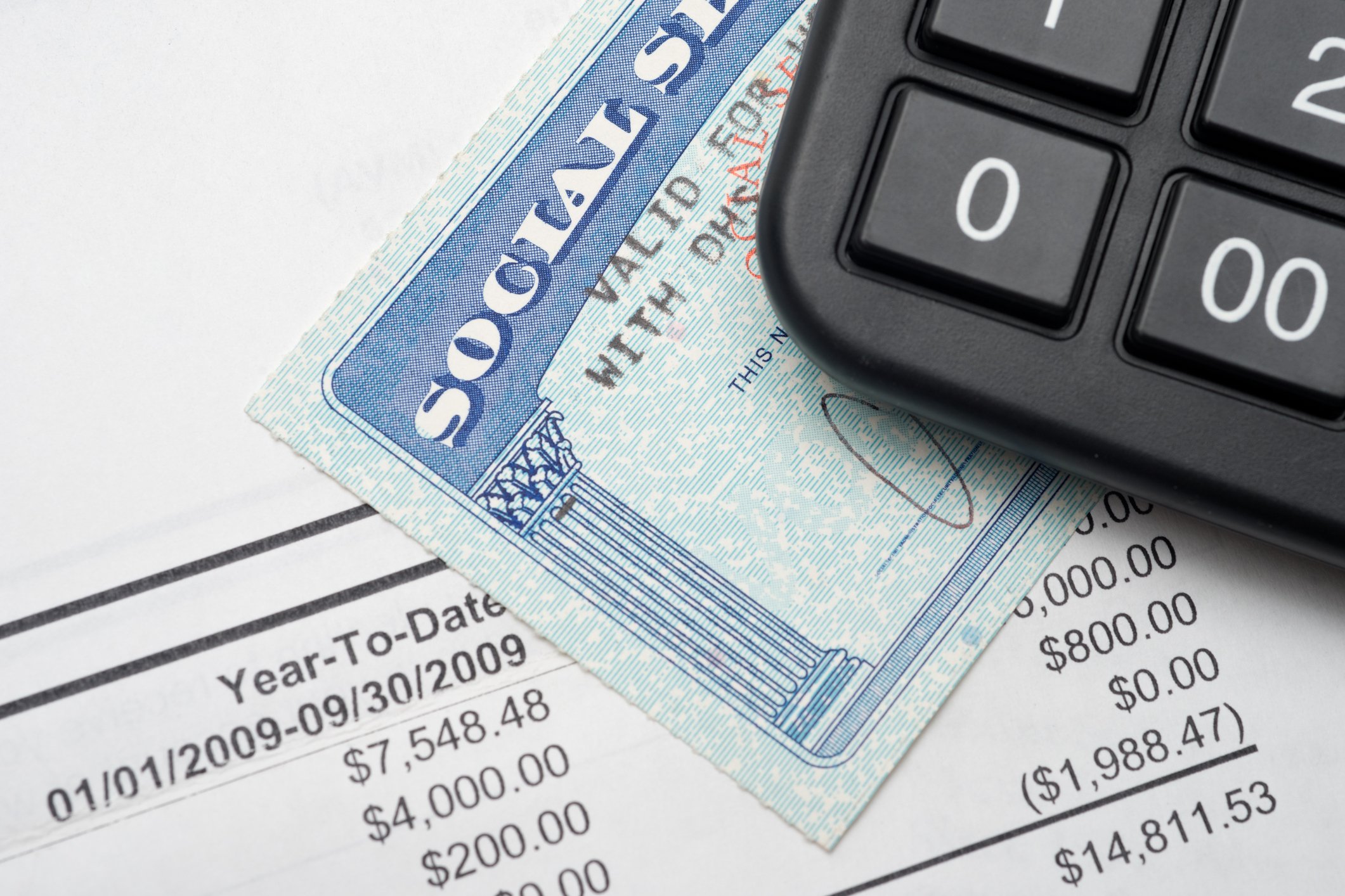 A Social Security card on top of a financial statement with a calculator on top of it.