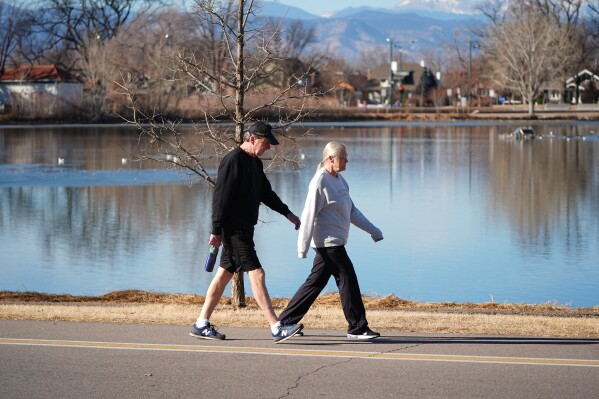 With a backdrop of snowless mountains, a couple walk around the lake in Washington Park, Friday, Feb. 6, 2026, in Denver. (AP Photo/David Zalubowski)