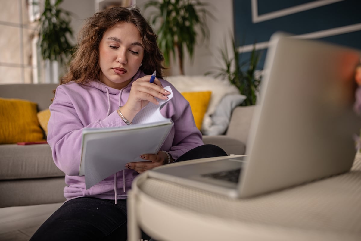 Student at home studying from notes while sitting in front of a laptop.