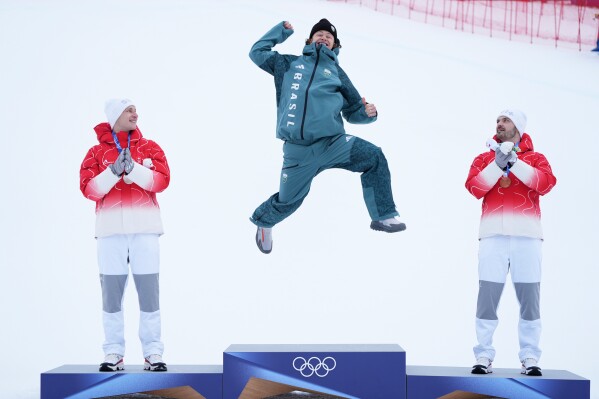 Brazil's Lucas Pinheiro Braathen celebrates winning a gold medal for an alpine ski men's giant slalom race, as silver medalist Switzerland's Marco Odermatt, right, and bronze medalist Switzerland's Loic Meillard applaud, at the 2026 Winter Olympics, in Bormio, Italy, Saturday, Feb. 14, 2026. (AP Photo/Rebecca Blackwell)