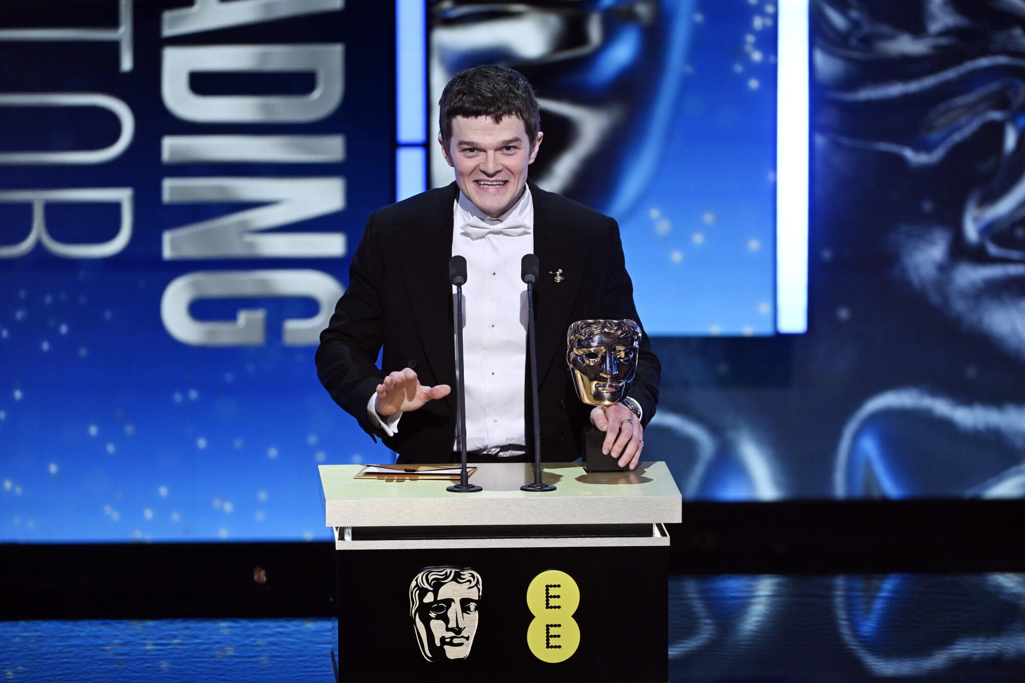 A man in a tuxedo smiles at a podium.