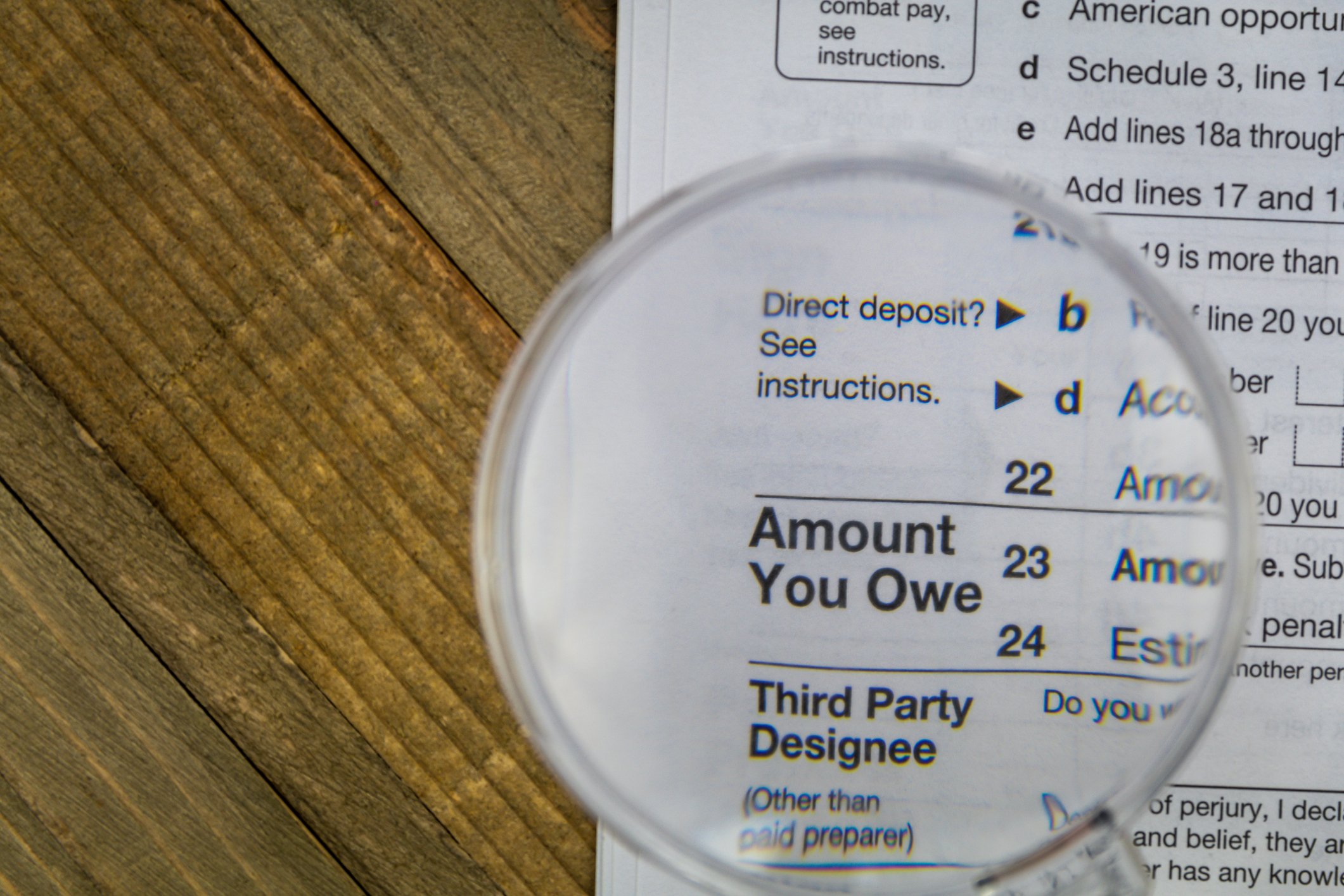 A magnifying glass held over an IRS tax form, which is enlarging the phrase, Amount You Owe.