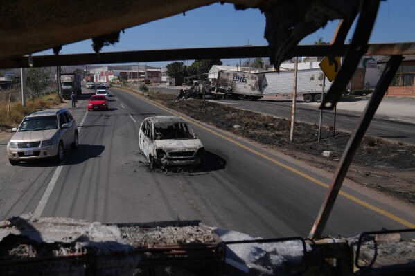 Vehicles pass a burned car a day after the Mexican army killed the leader of the Jalisco New Generation Cartel, Nemesio Oseguera Cervantes, known as "El Mencho," in Guadalajara, Mexico, Monday, Feb. 23, 2026. (AP Photo/Marco Ugarte)