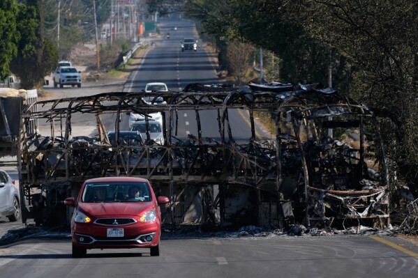 Vehicles drive past a charred bus the day after the Mexican army killed Jalisco New Generation Cartel leader Nemesio Oseguera Cervantes, known as "El Mencho," in Guadalajara, Mexico, Monday, Feb. 23, 2026. (AP Photo/Marco Ugarte)