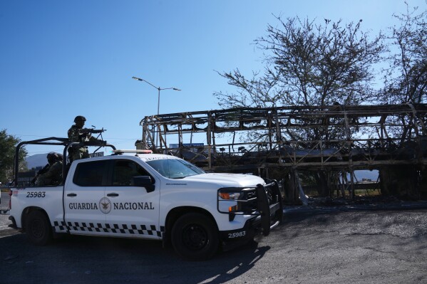 National Guard patrol past a charred vehicle the day after the Mexican army killed Jalisco New Generation Cartel leader Nemesio Oseguera Cervantes, known as "El Mencho," in Guadalajara, Mexico, Monday, Feb. 23, 2026. (AP Photo/Marco Ugarte)