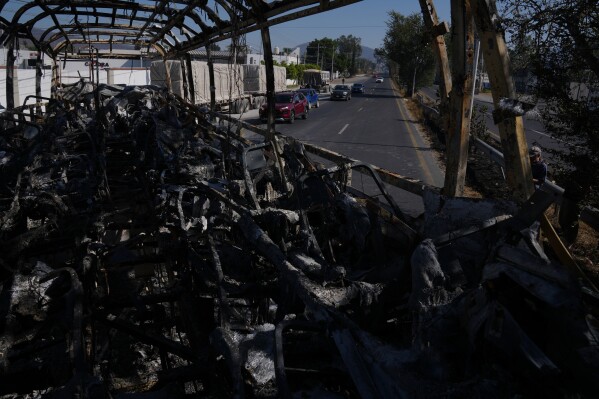 Vehicles drive past a charred bus the day after the Mexican army killed Jalisco New Generation Cartel leader Nemesio Oseguera Cervantes, known as "El Mencho," in Guadalajara, Mexico, Monday, Feb. 23, 2026. (AP Photo/Marco Ugarte)