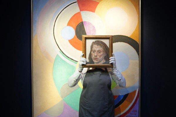 A staff member holds a painting "lb"created by British artist Lucian Freud, in front of the painting "Rythme couleur" created by French artist Sonia Delaunay, at the auction house Christie's in London, Wednesday, Feb. 25, 2026. The painting "lb" is estimated to sell for 1.2 - 1.8 million GBP (1.5 – 2.3 million USD) at Christie's 20th / 21st Century: London Evening Sale on March 5. (AP Photo/Kin Cheung)