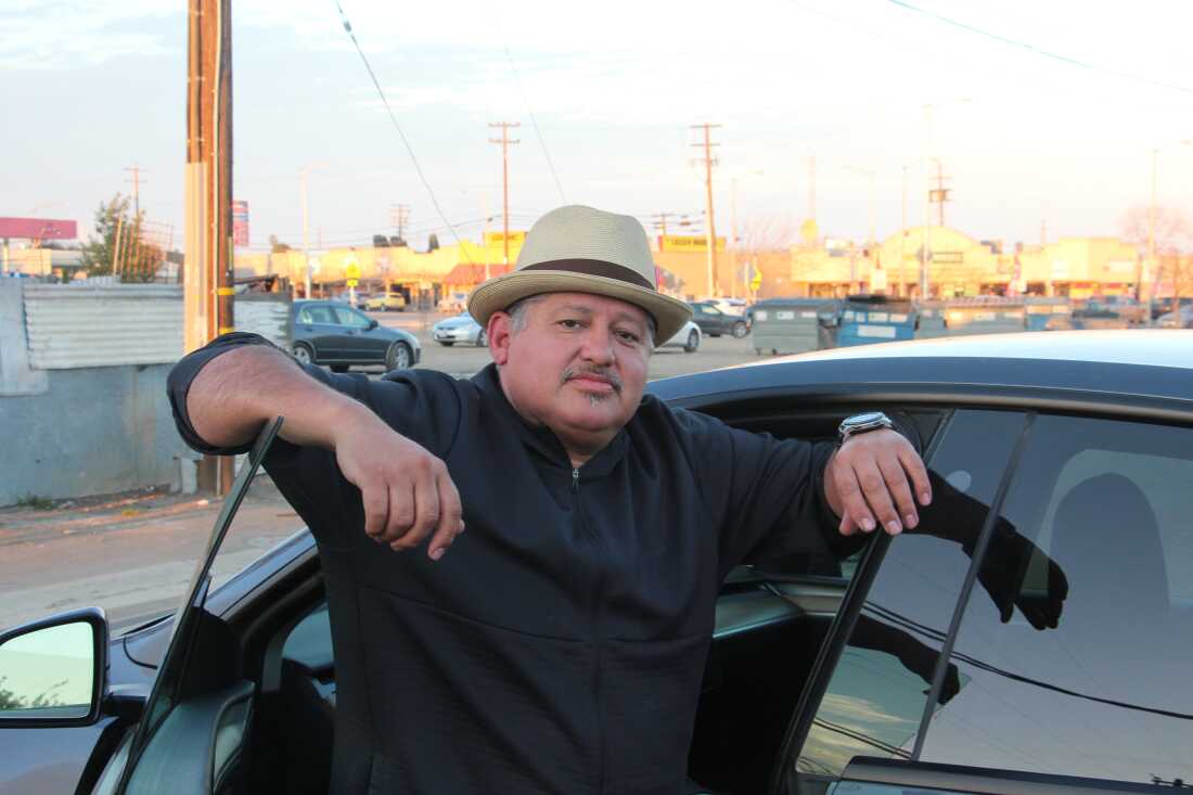A man wearing a hat leans in the open doorway of a car.