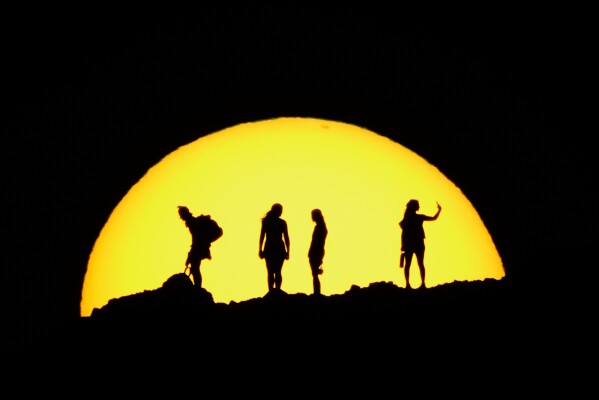 People are silhouetted against the setting sun while hiking at Papago park Wednesday, Feb. 25, 2026, in Phoenix. (AP Photo/Charlie Riedel)