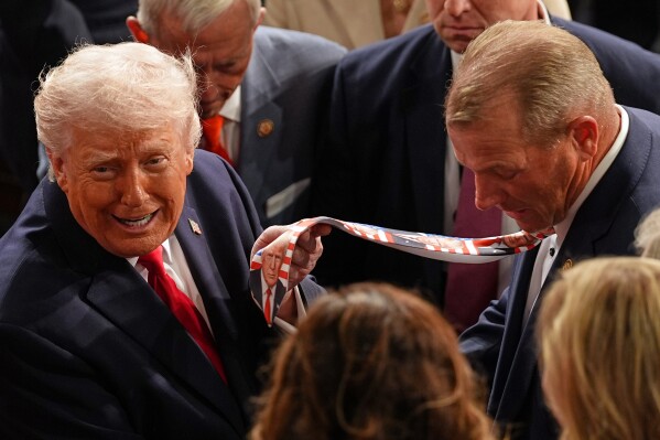 President Donald Trump holds up a tie designed with his face, worn by Rep. Troy Nehls, R-Texas, as he exits the House chamber after delivering the State of the Union address at the U.S. Capitol in Washington, Feb. 24, 2026. (AP Photo/Matt Rourke, File)