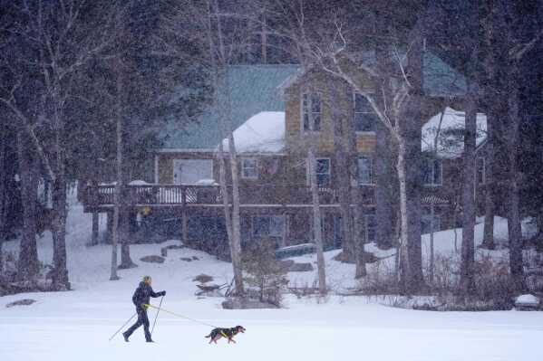 Cross-country skier Nate Andrew is pulled by his dog, Frankie, while traversing Moose Pond during a snowstorm in Bridgton, Maine, Feb. 25, 2026. (AP Photo/Robert F. Bukaty, File)