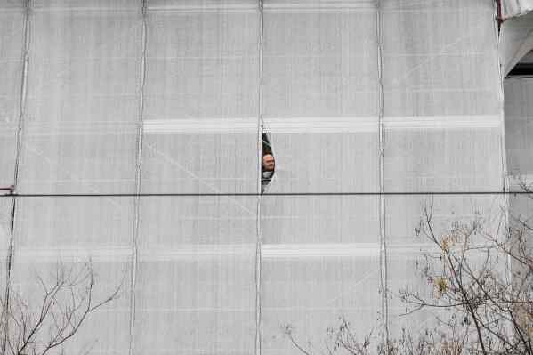 A construction worker peeks out from scaffolding as the Fendi Fall-Winter 2026-2027 women's fashion collection is presented in Milan, Italy, Feb. 25, 2026. (AP Photo/Luca Bruno, File)