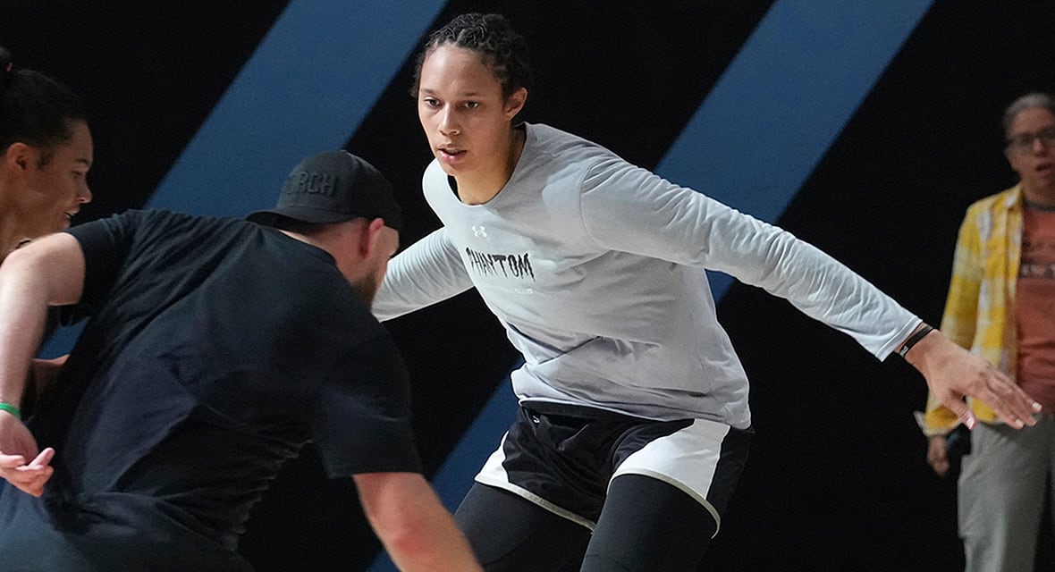 A woman in athletic gear plays basketball, facing off against a man in a dark shirt and baseball cap.