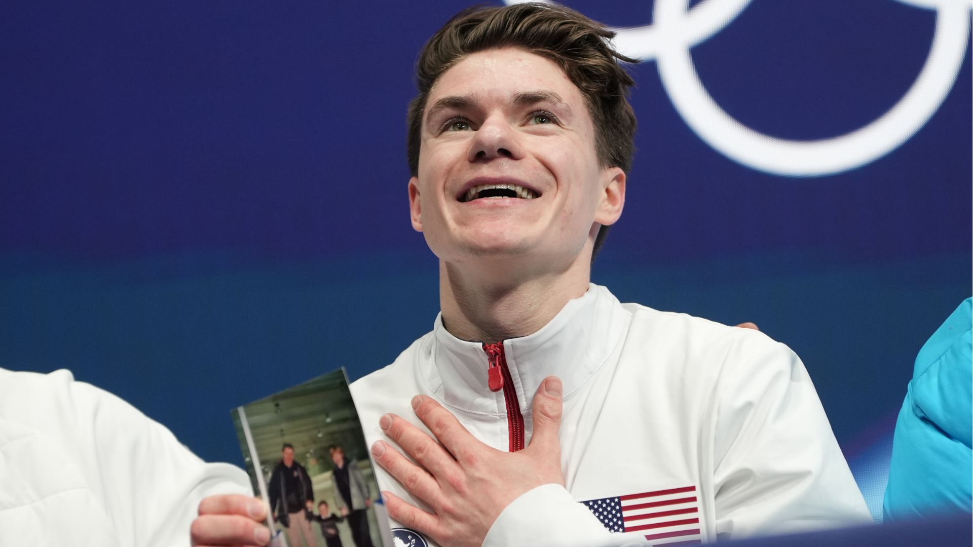 Maxim Naumov of the United States waits for his scores while holding a photo of his parents after competing during the men's figure skating short program at the 2026 Winter Olympics, in Milan, Italy, Tuesday, Feb. 10, 2026. 