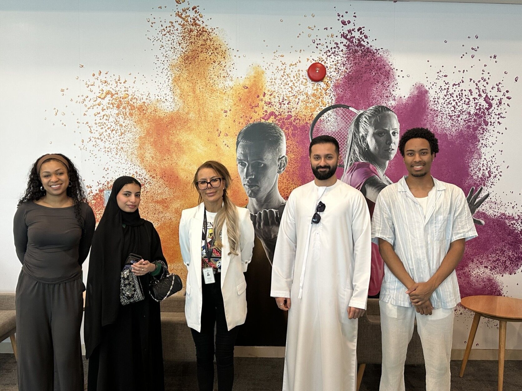 people stand for picture in front of wall with mural art of tennis player