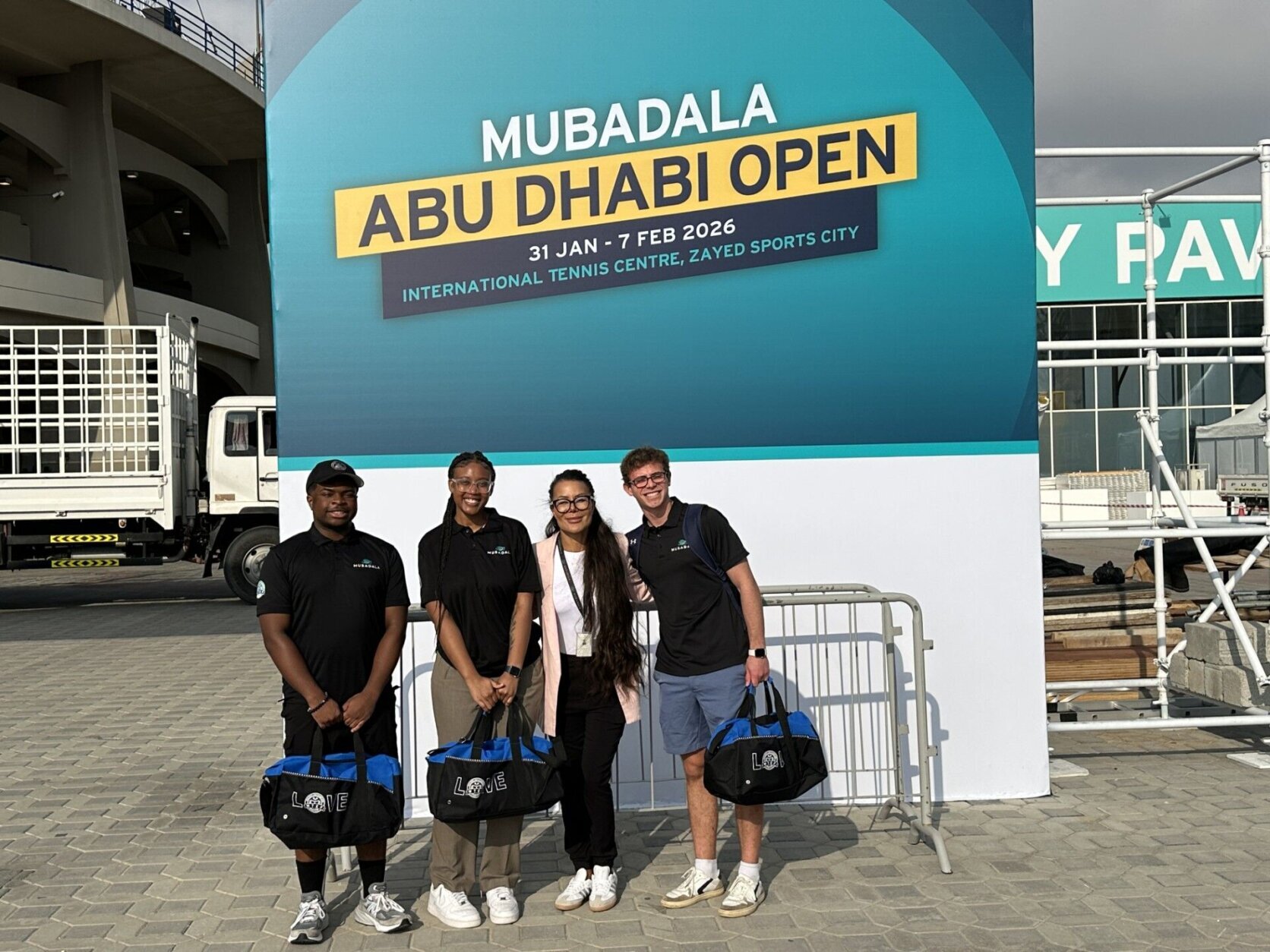 three young people standing holding duffel bags posing for picture below sign