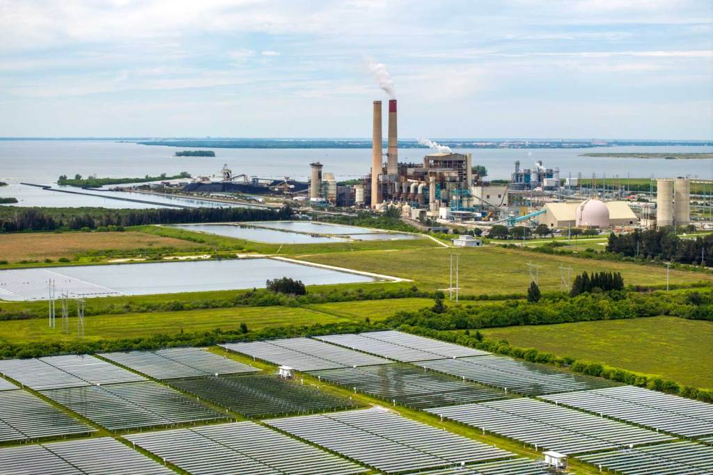 An overhead view of a power plant with a field of solar panels in the foreground 