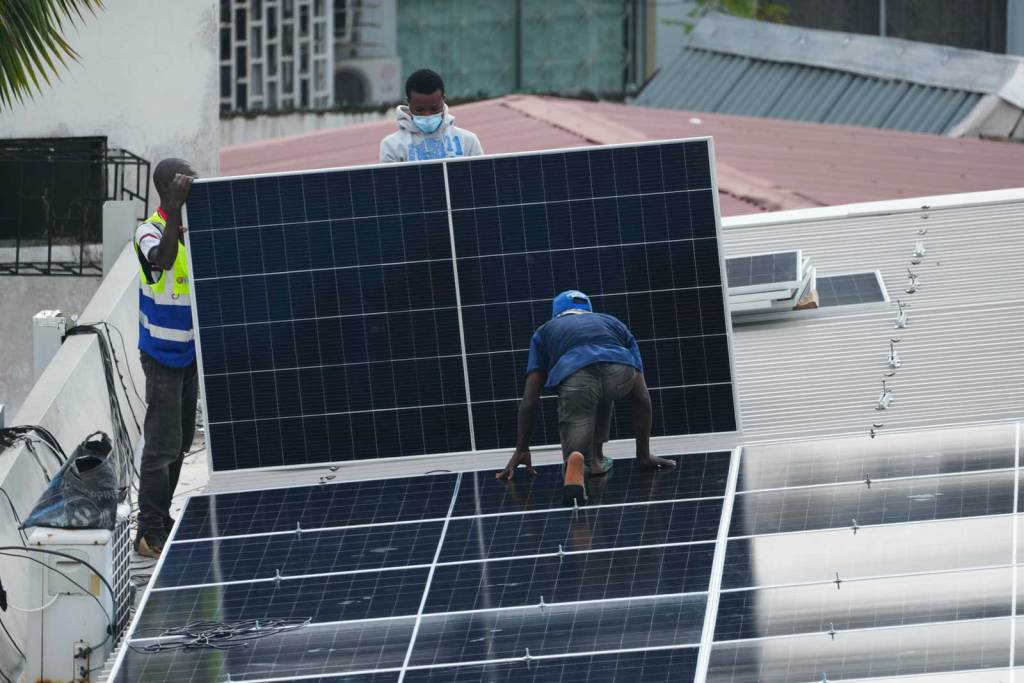 Three workers hold a solar panel on a roof 