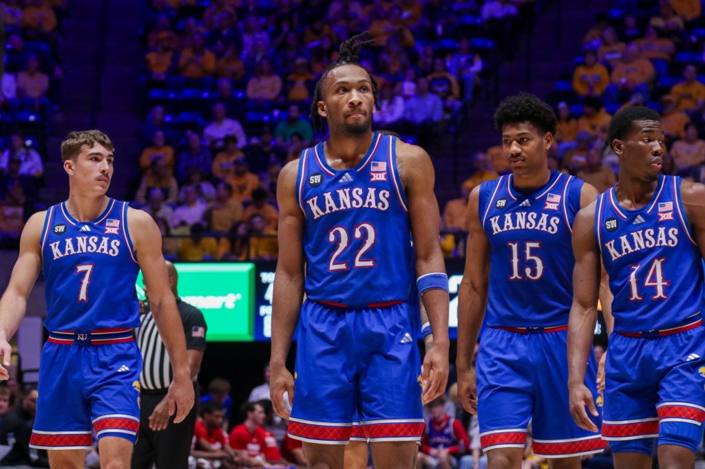 Four Kansas basketball players in blue uniforms standing on the court.