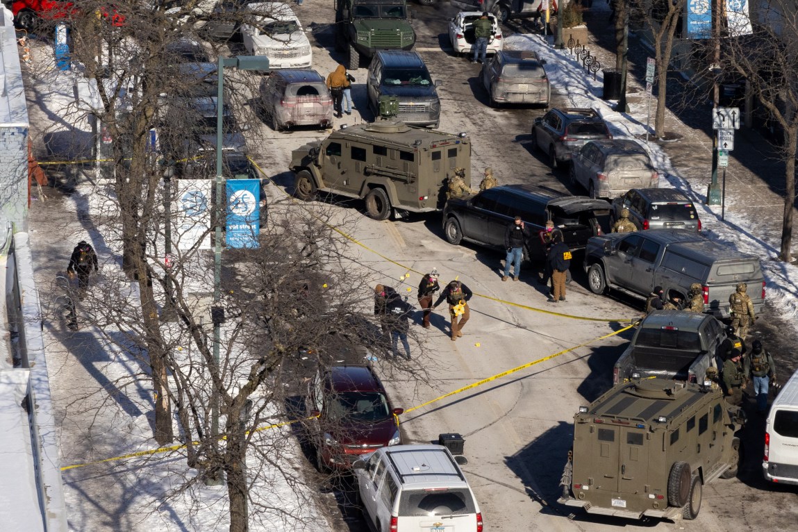 An overhead perspective of a street and sidewalks lined with trees. FBI agents walk around and inside an area marked off with caution tape. The area is blocked off by trucks and cars.